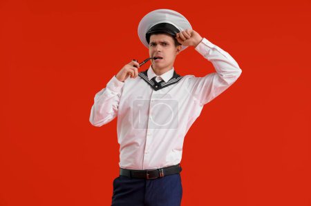 Thoughtful young sailor smoking pipe on red background