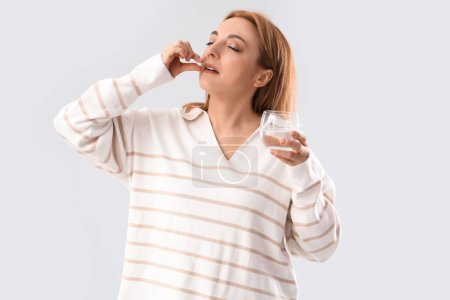 Mature woman taking pill on light background. Menopause concept