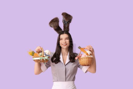 Happy female chambermaid in bunny ears with Easter baskets on purple background