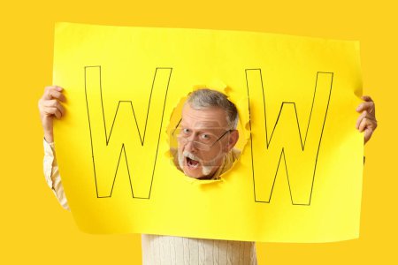 Shocked senior man holding poster with word WOW on yellow background