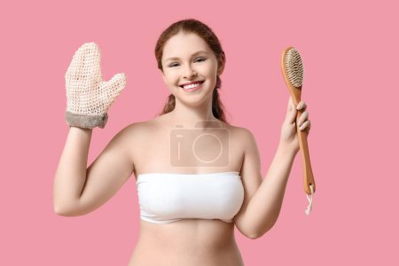 Schöne junge glückliche Frau mit Badehandschuh und Massagebürste auf rosa Hintergrund