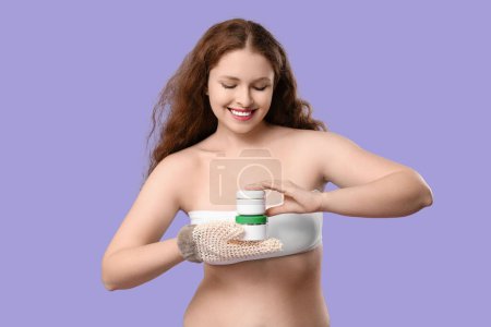 Schöne junge glückliche Frau mit Badehandschuhen und Cremegläsern auf violettem Hintergrund