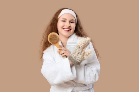 Schöne junge glückliche Frau im Bademantel mit Badehandschuh auf braunem Hintergrund