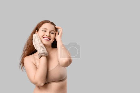 Schöne junge glückliche Frau mit Badehandschuh auf grauem Hintergrund