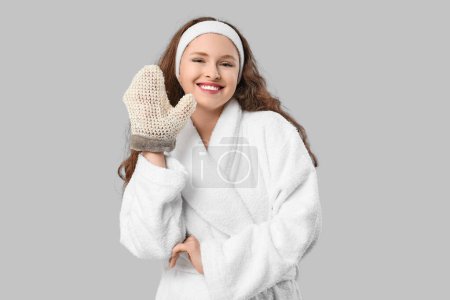 Schöne junge glückliche Frau im Bademantel mit Badehandschuh auf grauem Hintergrund
