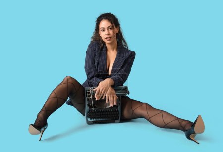 Attractive African-American secretary with vintage typewriter sitting on blue background