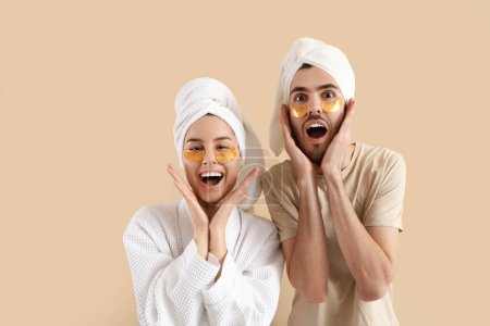 Surprised young couple after shower with under-eye patches on beige background