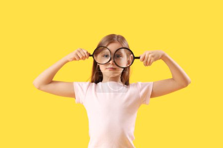 Funny little girl with magnifiers on yellow background