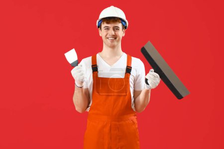Male decorator with putty knives on red background