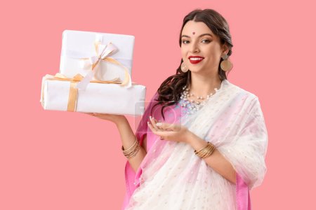 Téléchargez les photos : Belle jeune femme indienne en sari avec des boîtes-cadeaux sur fond rose - en image libre de droit