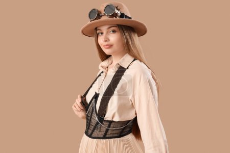 Stylish young woman in steampunk goggles on beige background