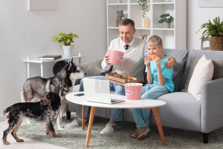 Mature doctor with his little son and dogs watching movie on laptop at home