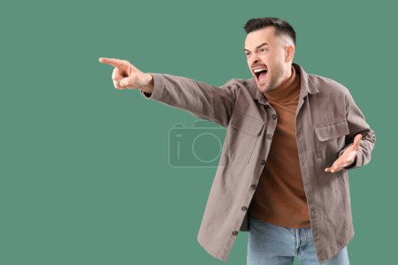 Photo for Angry young man pointing at something on green background. Accusation concept - Royalty Free Image
