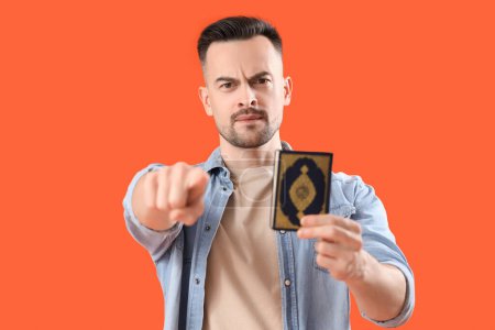 Photo for Young man with Koran pointing at viewer on orange background, closeup. Accusation concept - Royalty Free Image