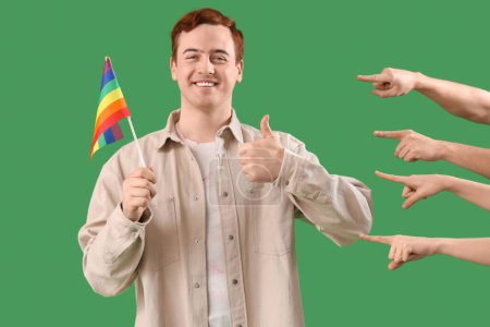 Photo for People pointing at young man with LGBT flag showing thumb-up on green background. Accusation concept - Royalty Free Image