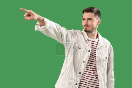 Photo for Young man pointing at something on green background. Accusation concept - Royalty Free Image