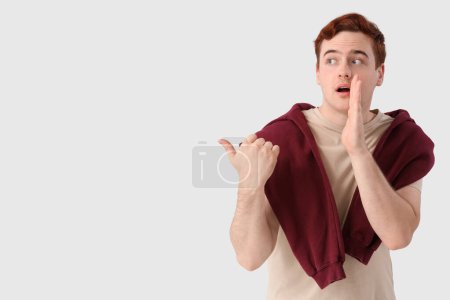 Photo for Gossiping young man pointing at something on white background. Accusation concept - Royalty Free Image