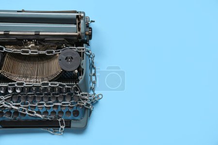 Vintage typewriter with chains on blue background. Printing ban concept