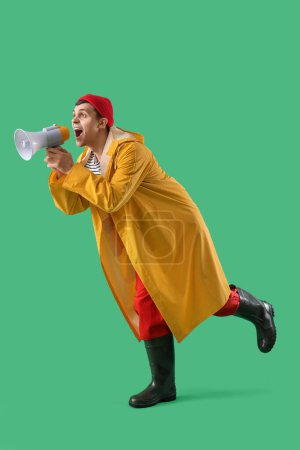 Photo for Young sailor in raincoat shouting into megaphone on green background - Royalty Free Image