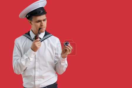 Thoughtful young sailor with compass smoking pipe on red background