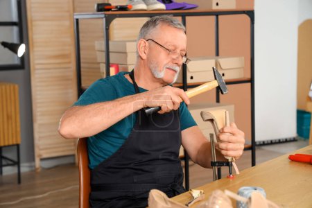Téléchargez les photos : Mature cordonnier réparer talon cassé à la table dans l'atelier - en image libre de droit