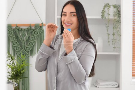 Téléchargez les photos : Belle jeune femme heureuse avec fil dentaire dans la salle de bain à la maison - en image libre de droit
