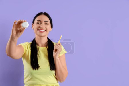 Téléchargez les photos : Belle jeune femme heureuse avec fil dentaire et brosse à dents sur fond violet - en image libre de droit