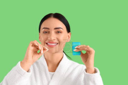 Téléchargez les photos : Belle jeune femme heureuse en peignoir avec fil dentaire sur fond vert - en image libre de droit
