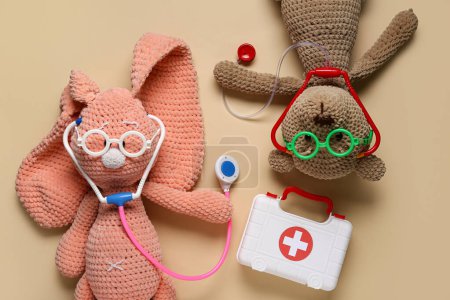 Photo for Toy first aid kit with teddy bear, toy bunny and stethoscope on beige background. Top view - Royalty Free Image