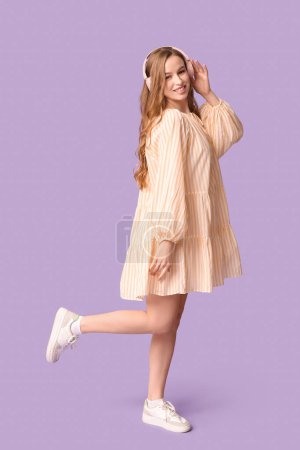 Happy young woman in headphones on lilac background