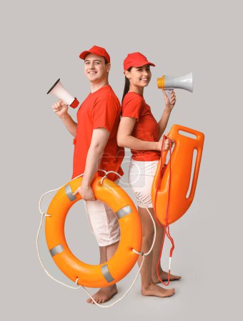 Lifeguards with ring buoy, rescue tube and megaphones on grey background