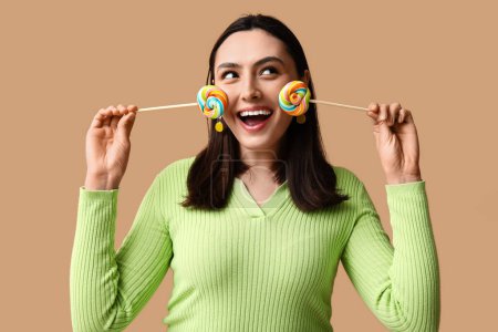 Foto de Mujer joven feliz con piruletas dulces sobre fondo marrón - Imagen libre de derechos