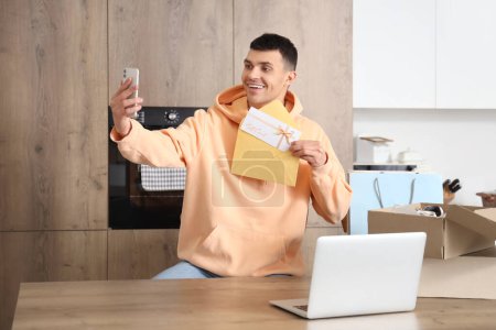 Junger Mann mit Gutschein im Umschlag macht Selfie zu Hause
