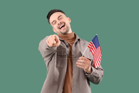 Rire jeune homme avec le drapeau des États-Unis pointant vers le spectateur sur fond vert. Concept d'accusation