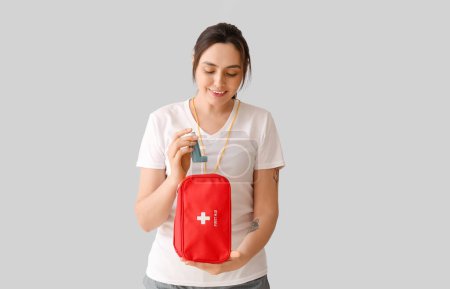 Sporty young woman with inhaler and first aid kit on light background