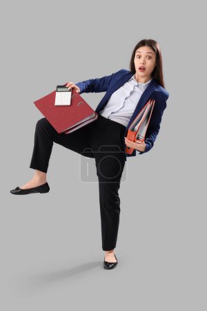 Foto de Funny sorprendió a la mujer de negocios asiática con carpetas y calculadora sobre fondo gris - Imagen libre de derechos