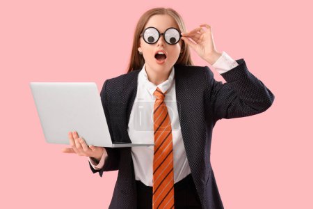 Foto de Joven mujer de negocios sorprendido en disfraz divertido con el ordenador portátil sobre fondo rosa - Imagen libre de derechos