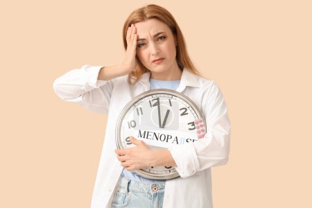 Mature woman holding paper with word MENOPAUSE and clock on beige background