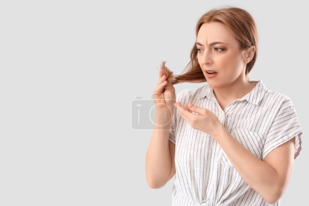 Upset mature woman with thin hair on light background. Menopause concept