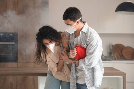 Young couple with first aid kit escaping from burning kitchen