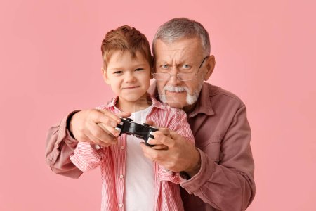 Photo for Grandfather with his happy cute little grandson playing video games on pink background - Royalty Free Image