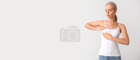 Foto de Mujer joven revisando su pecho sobre fondo claro con espacio para el texto. Concepto de concienciación - Imagen libre de derechos