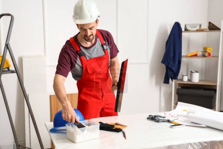 Male decorator with putty knives working in room