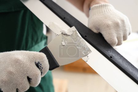 Male decorator with putty knives working in room, closeup