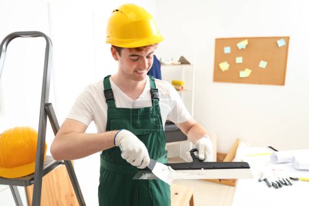 Téléchargez les photos : Décorateur masculin avec couteaux à mastic travaillant dans la chambre - en image libre de droit