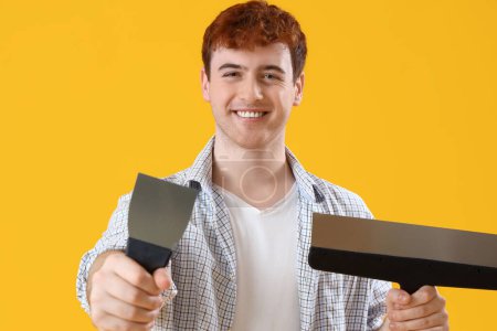 Young man with putty knives on yellow background