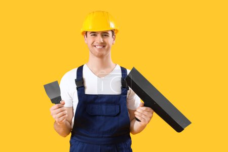 Téléchargez les photos : Décorateur masculin avec couteaux à mastic sur fond jaune - en image libre de droit