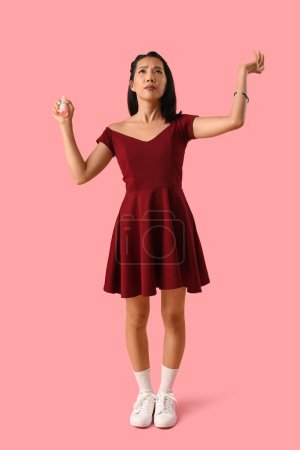 Young Asian woman with mosquito repellent on pink background