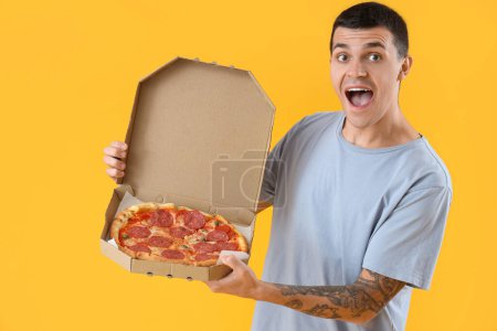Photo for Surprised young man with tasty pepperoni pizza on yellow background - Royalty Free Image