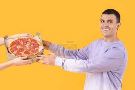 Junger Mann nimmt leckere Pfefferoni-Pizza auf gelbem Hintergrund